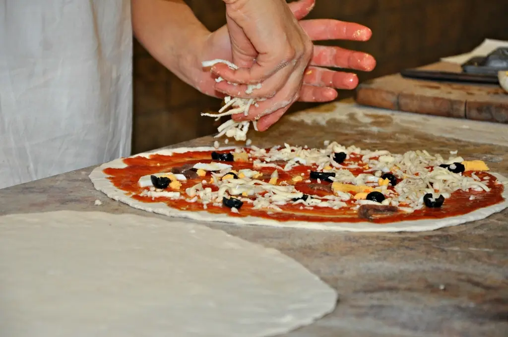 Au banc, les mains garnissent une pizza avant le four