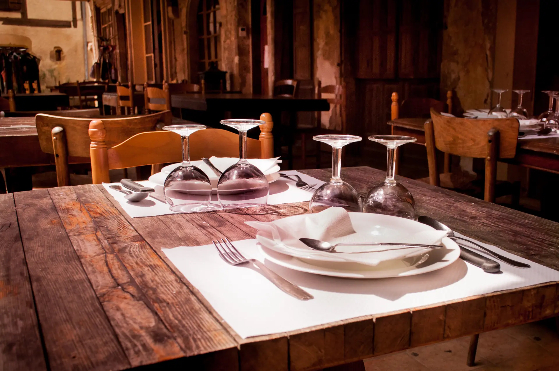 Une table de bois dressée, les verres retournés, avant le service